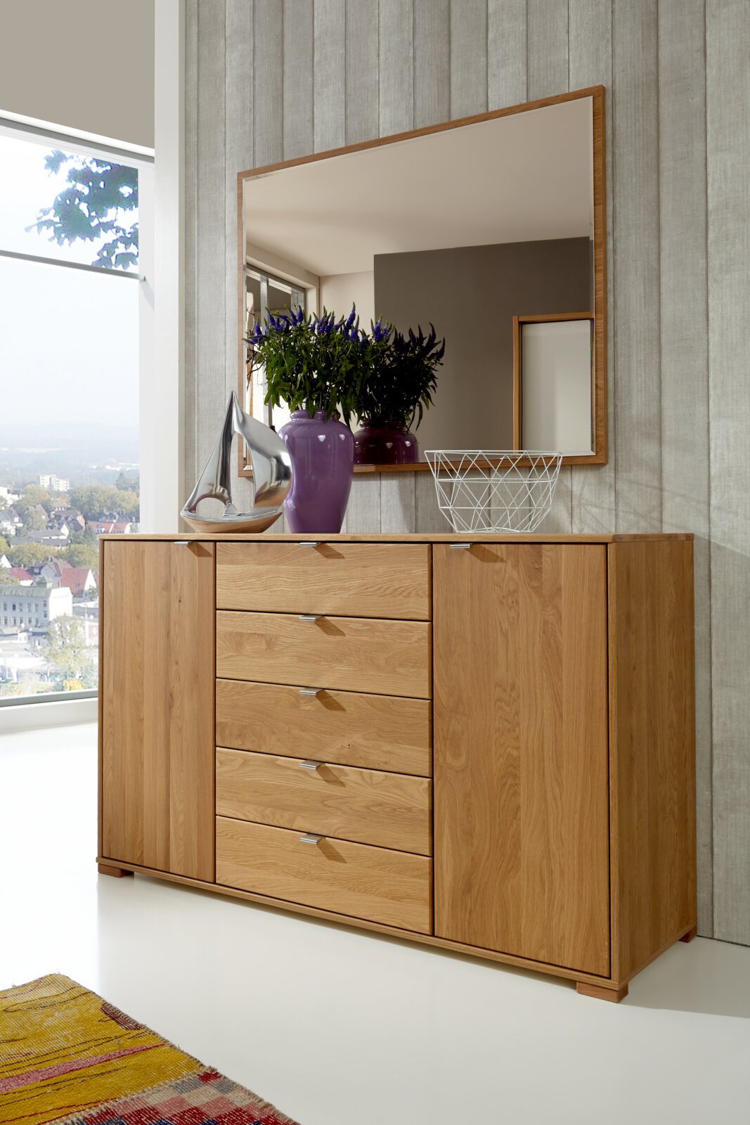 Schubkastenkommode aus Holz mit fünf Schubladen und zwei Türen, dekoriert mit einer lila Vase und einem silbernen Segelboot, aus der Frontalperspektive fotografiert.