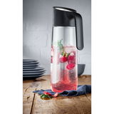 Wasserkaraffe Nuro mit Griff, gefüllt mit Wasser und roten Früchten, auf einem Holztisch stehend, seitliche Perspektive