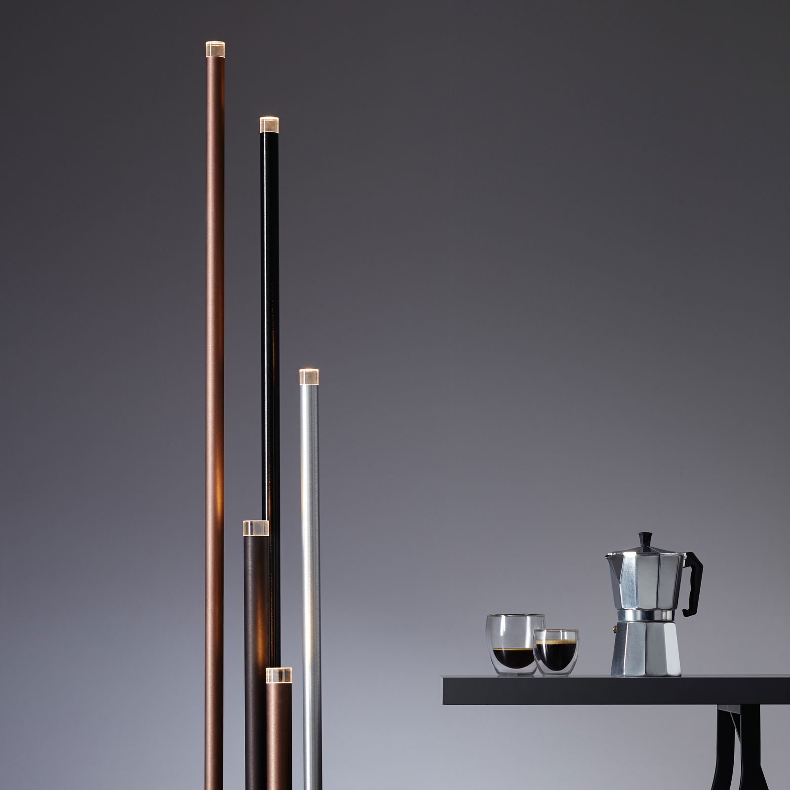 Mehrere schlanke, vertikale LED-Leuchten in verschiedenen Farben neben einem Tisch mit einer Kaffeekanne und Gläsern, seitliche Perspektive.