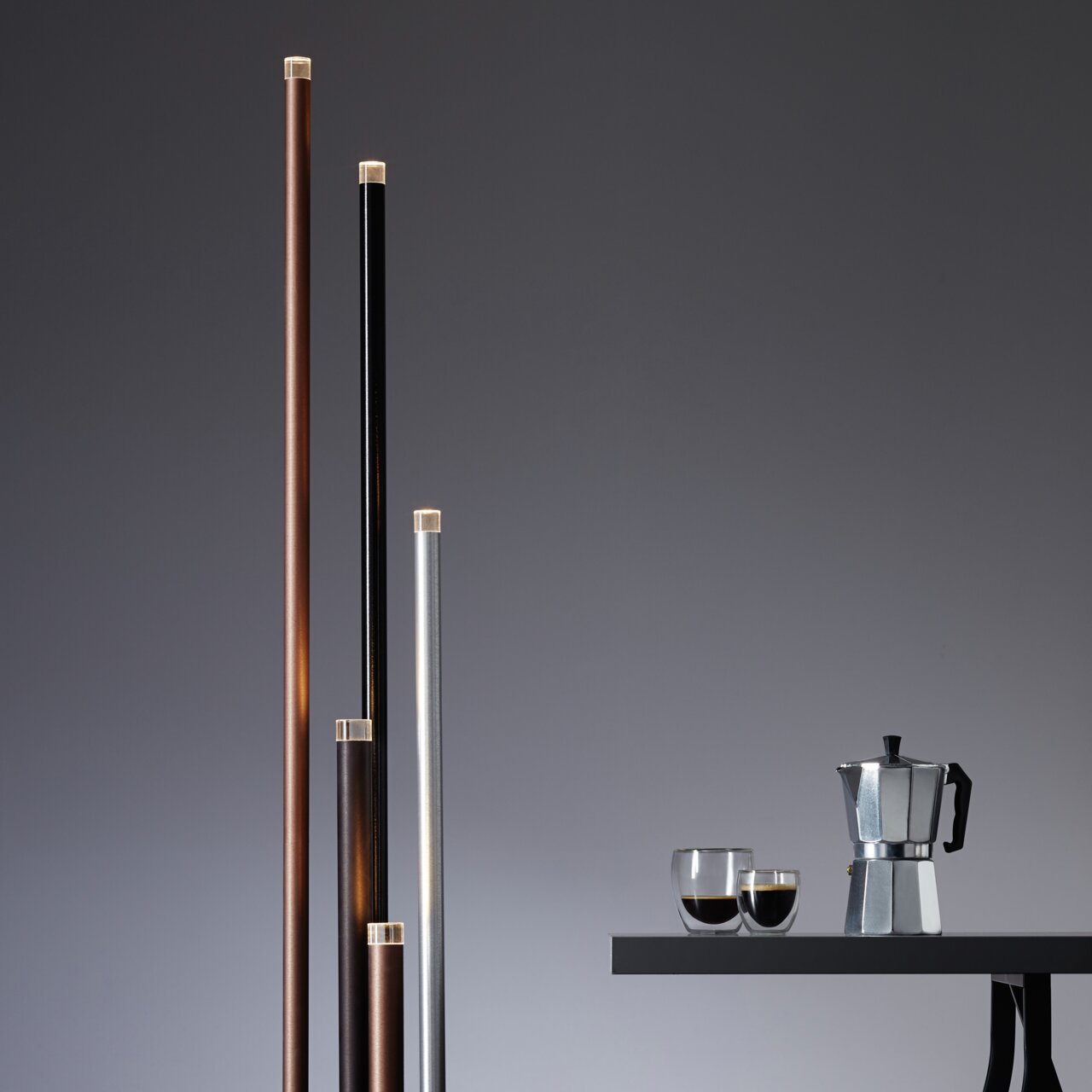 Mehrere schlanke, vertikale LED-Leuchten in verschiedenen Farben neben einem Tisch mit einer Kaffeekanne und Gläsern, seitliche Perspektive.