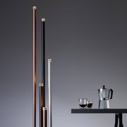 Mehrere schlanke, vertikale LED-Leuchten in verschiedenen Farben neben einem Tisch mit einer Kaffeekanne und Gläsern, seitliche Perspektive.