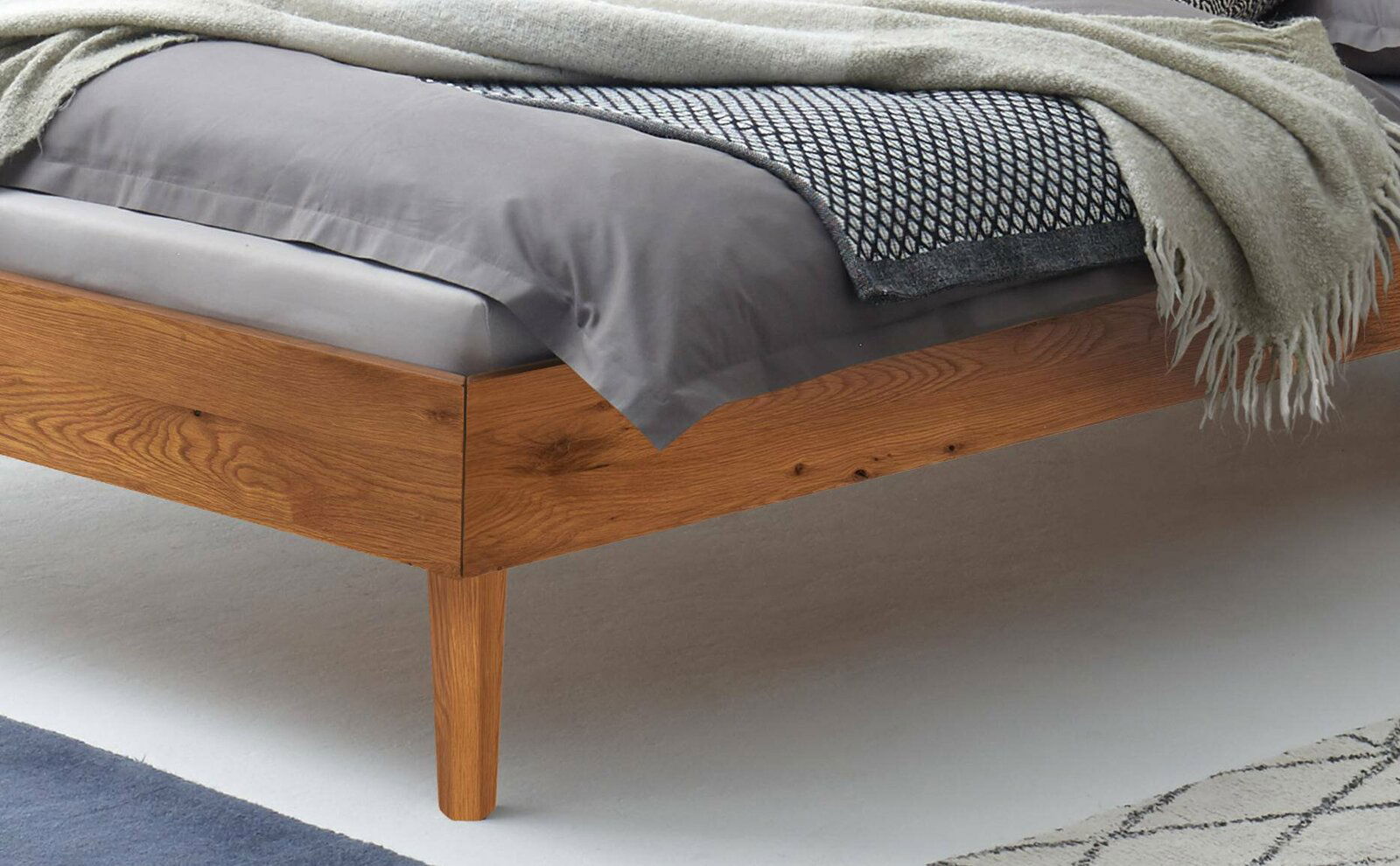 Nahaufnahme eines Bettgestells aus Holz mit Bettwäsche und Decken, seitliche Perspektive