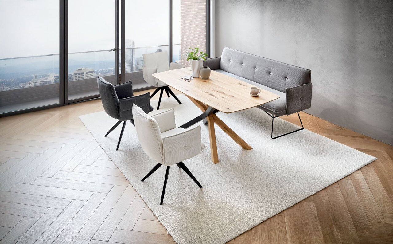 Novel Armlehnstuhl COCO Moderne Esszimmermöbel in einem hellen Raum mit Blick auf die Stadt, bestehend aus einem Holztisch, grauen und weißen Armlehnstühlen sowie einer grauen Bank. Perspektive von schräg oben.