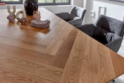 Nahaufnahme eines Esstisches mit Fischgrätenmuster aus Holz, dekoriert mit modernen Keramikvasen und Stoffservietten, umgeben von grauen Stühlen.