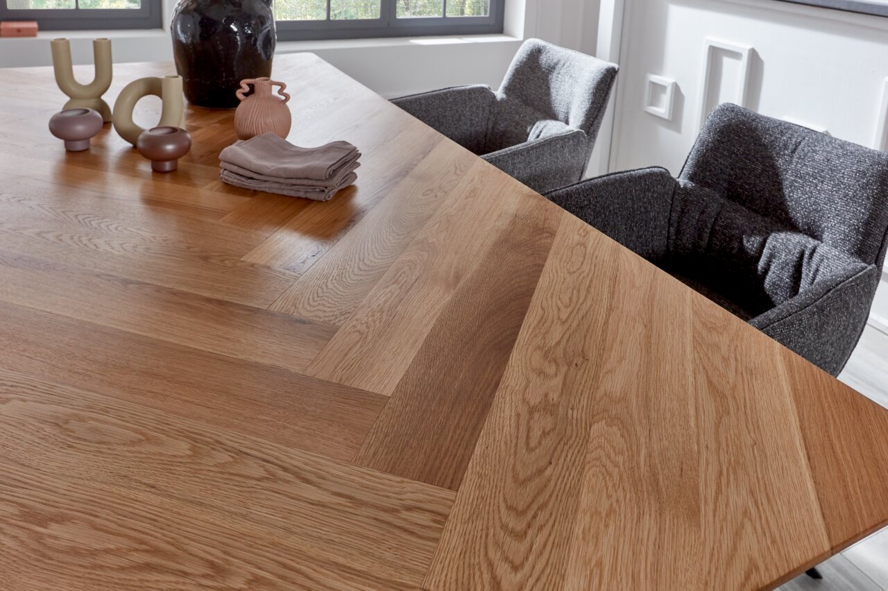 Nahaufnahme eines Esstisches mit Fischgrätenmuster aus Holz, dekoriert mit modernen Keramikvasen und Stoffservietten, umgeben von grauen Stühlen.