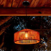 Leuchtende Pendelleuchte mit orangefarbenem, geflochtenem Lampenschirm und schwarzem Kabel unter einer Holzdecke, Ansicht leicht von unten (Untersicht).