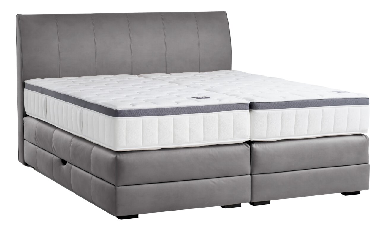 Boxspringbett in seitlicher Perspektive mit grauem Polster und weißer Matratze