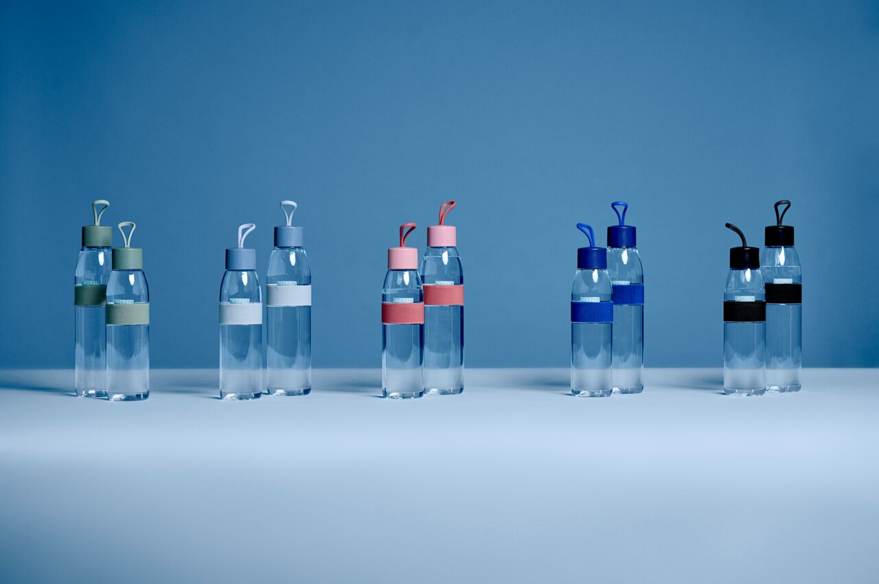 Mehrere transparente Trinkflaschen mit bunten Deckeln und Bändern, frontal auf einem blauen Hintergrund präsentiert.