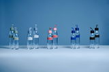 Mehrere transparente Trinkflaschen mit bunten Deckeln und Bändern, frontal auf einem blauen Hintergrund präsentiert.