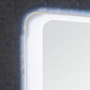 Nahaufnahme eines Spiegelelements mit abgerundeten Ecken und integrierter Hintergrundbeleuchtung, seitliche Perspektive.