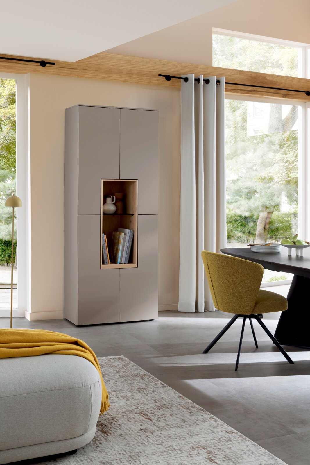 Schöner Wohnen Vitrine met 4 deuren CREDENZA Moderne hoge opbergkast in matgrijs met open nis in houtlook en glazen plank, gefotografeerd in een lichte woonkamer vanuit een schuin vooraanzicht.