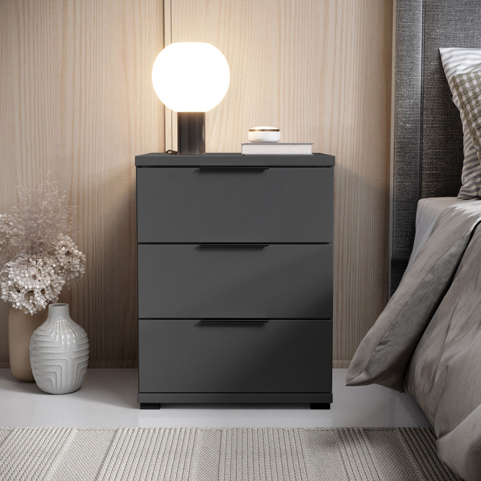 Z2 Nachtkommode SMILLA 2 Moderne Nachtkommode mit drei Schubladen in dunklem Design, seitliche Perspektive, dekoriert mit Lampe und Vasen.