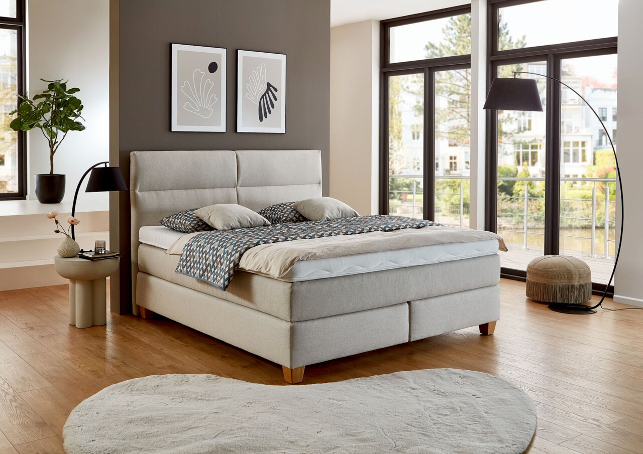 Modernes Boxspringbett in einem stilvollen Schlafzimmer mit großen Fenstern, seitliche Perspektive
