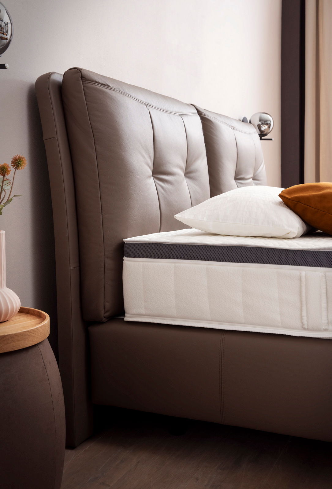 Nahaufnahme eines Boxspringbetts mit braunem, gepolstertem Kopfteil und weißer Matratze, seitliche Perspektive.