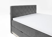 Graues Boxspringbett mit gestepptem Kopfteil, seitliche Perspektive