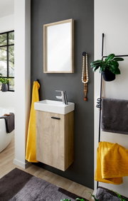 Modernes Badezimmer-Waschtischset mit wandhängendem Unterschrank in heller Holzoptik, weißem rechteckigem Aufsatzbecken, Chrom-Armatur und Spiegel mit Holzrahmen an dunkelgrauer Wand, fotografiert in leichter Seitenansicht von vorne.
