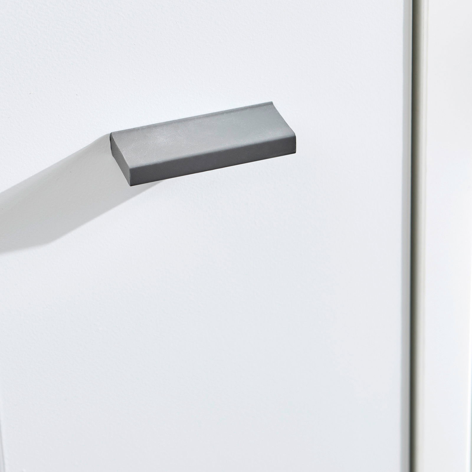 Nahaufnahme eines grauen Griffs an einer weißen Kommode, seitliche Perspektive
