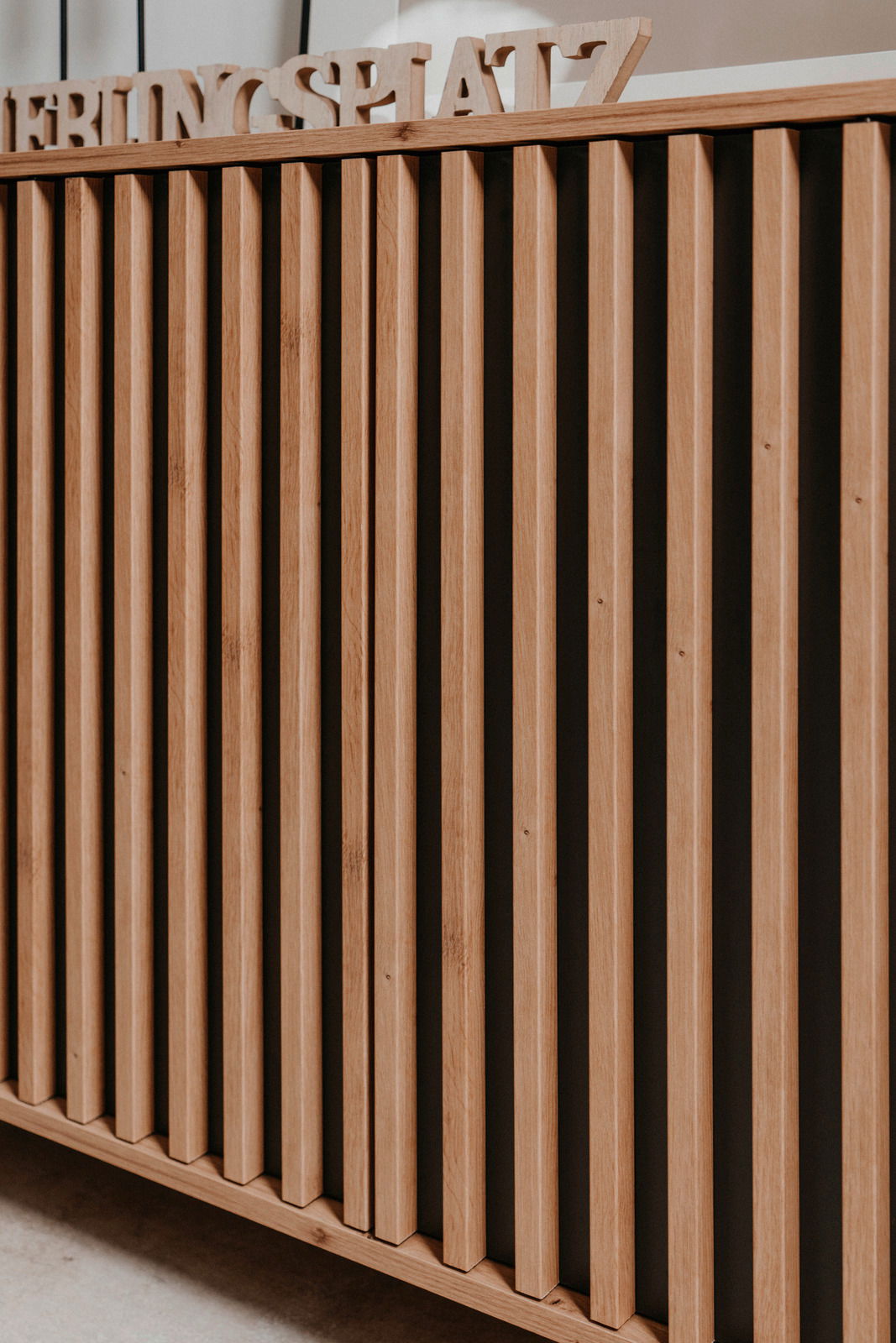 Nahaufnahme einer Kommode mit vertikalen Holzlatten und dekorativem Schriftzug auf der Oberseite, seitliche Perspektive