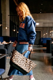 Een vrouw in een blauw jasje en een spijkerrok draagt een boodschappenmand met luipaardprint in een modern restaurant, gezien vanuit een zijdelingse hoek.
