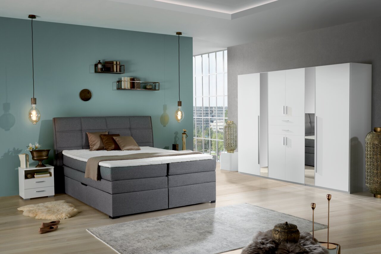 Moderner weißer Drehtürenschrank mit sechs Türen in einem stilvoll eingerichteten Schlafzimmer, seitliche Perspektive.