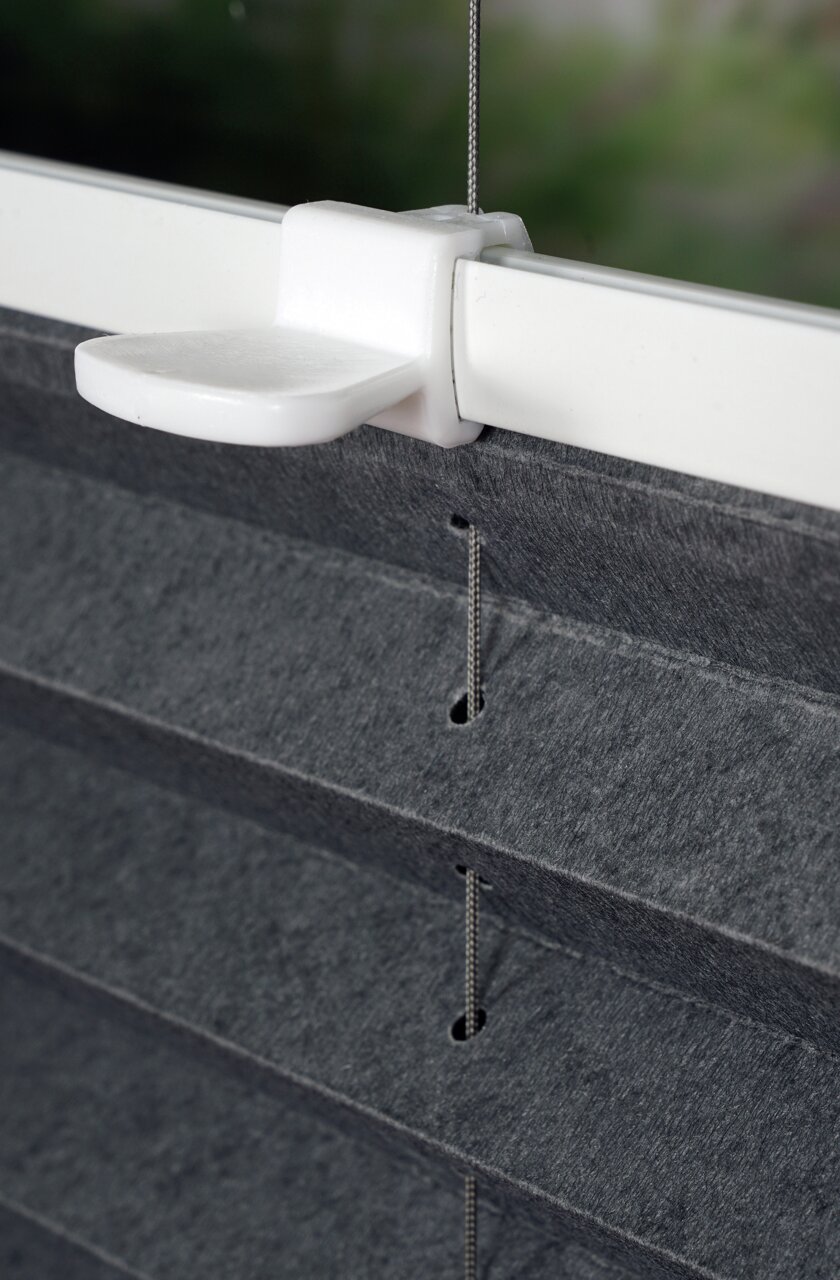 Nahaufnahme eines grauen, gefädelten Plissees mit weißer Halterung an einem Fensterrahmen.