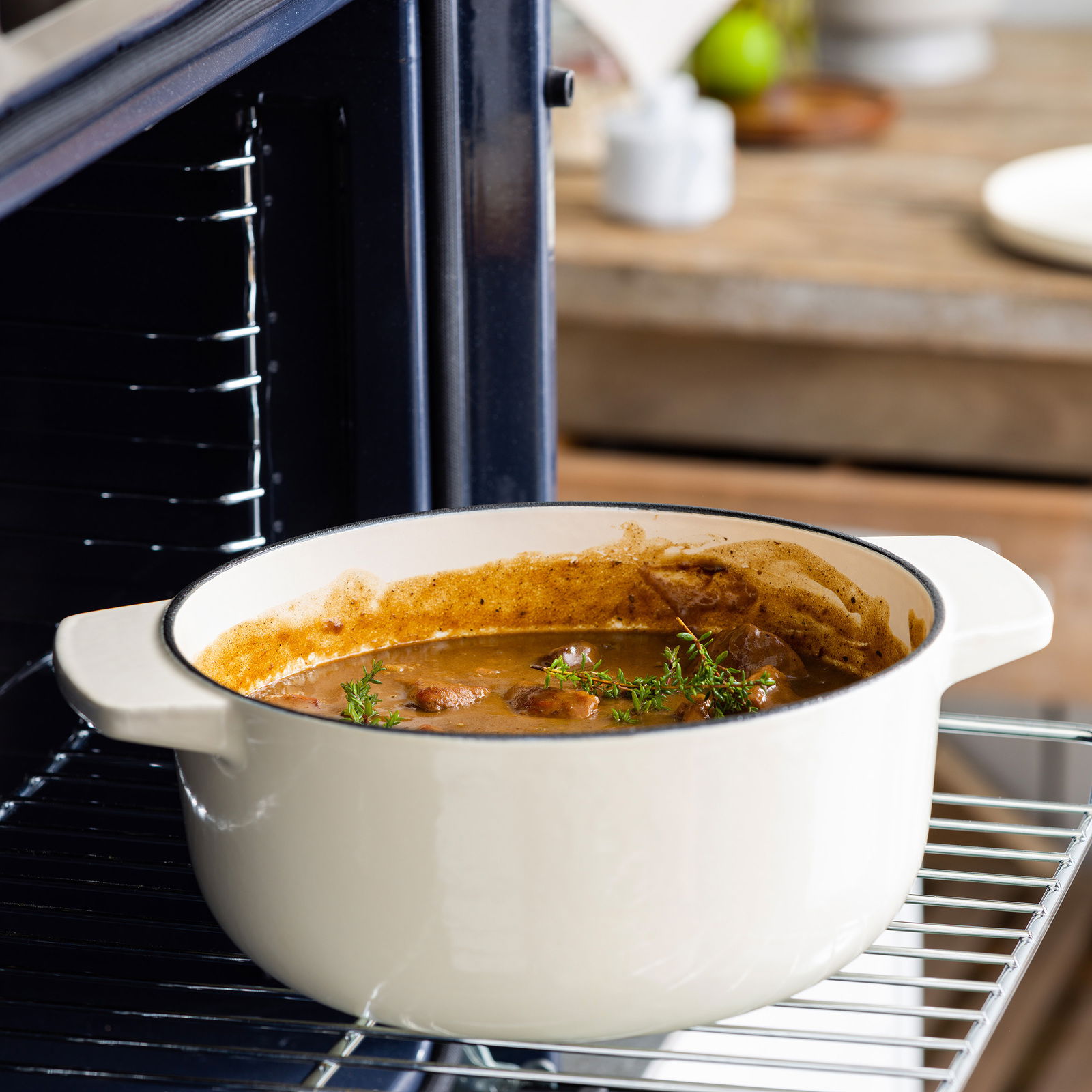 Gusseisen Bräter 26cm in Mandel-Farbe, gefüllt mit einem Eintopf, im Ofen auf einem Gitterrost von der Seite fotografiert.