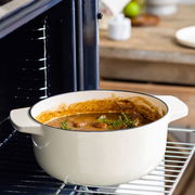 Gusseisen Bräter 26cm in Mandel-Farbe, gefüllt mit einem Eintopf, im Ofen auf einem Gitterrost von der Seite fotografiert.