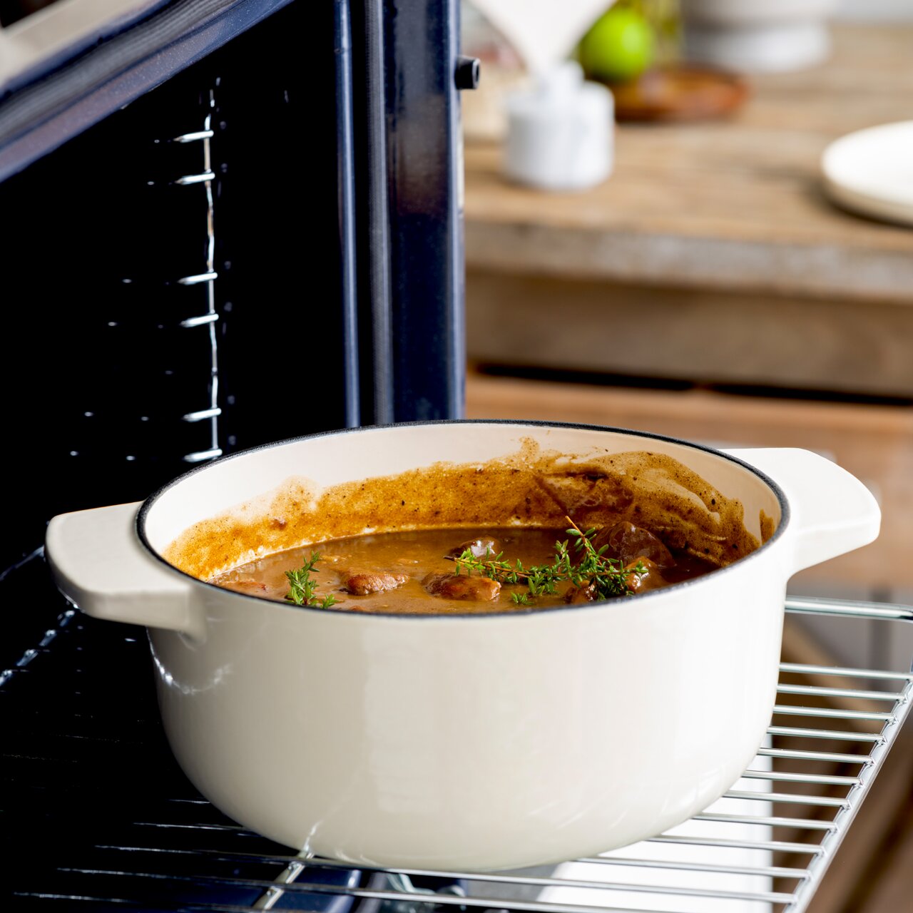 Gusseisen Bräter 26cm in Mandel-Farbe, gefüllt mit einem Eintopf, im Ofen auf einem Gitterrost von der Seite fotografiert.