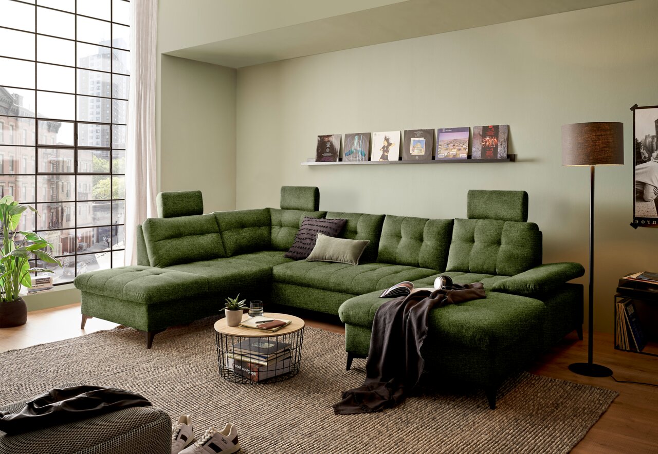 Groene hoekbank in U-vorm in een moderne woonkamer met grote ramen, gezien vanaf de voorkant.