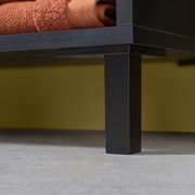 Nahaufnahme eines schwarzen Waschbeckenunterschranks mit Metallbeinen und einem orangefarbenen Handtuch, seitliche Perspektive.