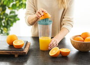 Frau presst eine Orange mit einem grünen Küchenhelfer auf einem Tisch aus, seitliche Perspektive.