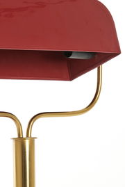 Nahaufnahme einer Tischleuchte mit rotem Schirm und goldfarbenem Gestell, seitliche Perspektive