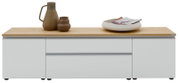 Modernes Lowboard/TV-Board mit weißer Front und heller Holzplatte, mittig Schublade und seitlichen Fächern, frontal von vorne fotografiert; auf der Platte Keramikvase, kleines Gefäß und Schale mit Zeitschriften.