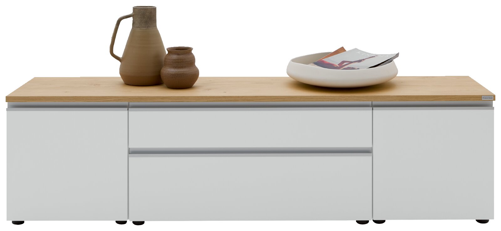 Modernes Lowboard/TV-Board mit weißer Front und heller Holzplatte, mittig Schublade und seitlichen Fächern, frontal von vorne fotografiert; auf der Platte Keramikvase, kleines Gefäß und Schale mit Zeitschriften.