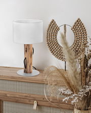 Tischleuchte mit Holzfuß und weißem Lampenschirm auf einer Kommode, seitliche Perspektive