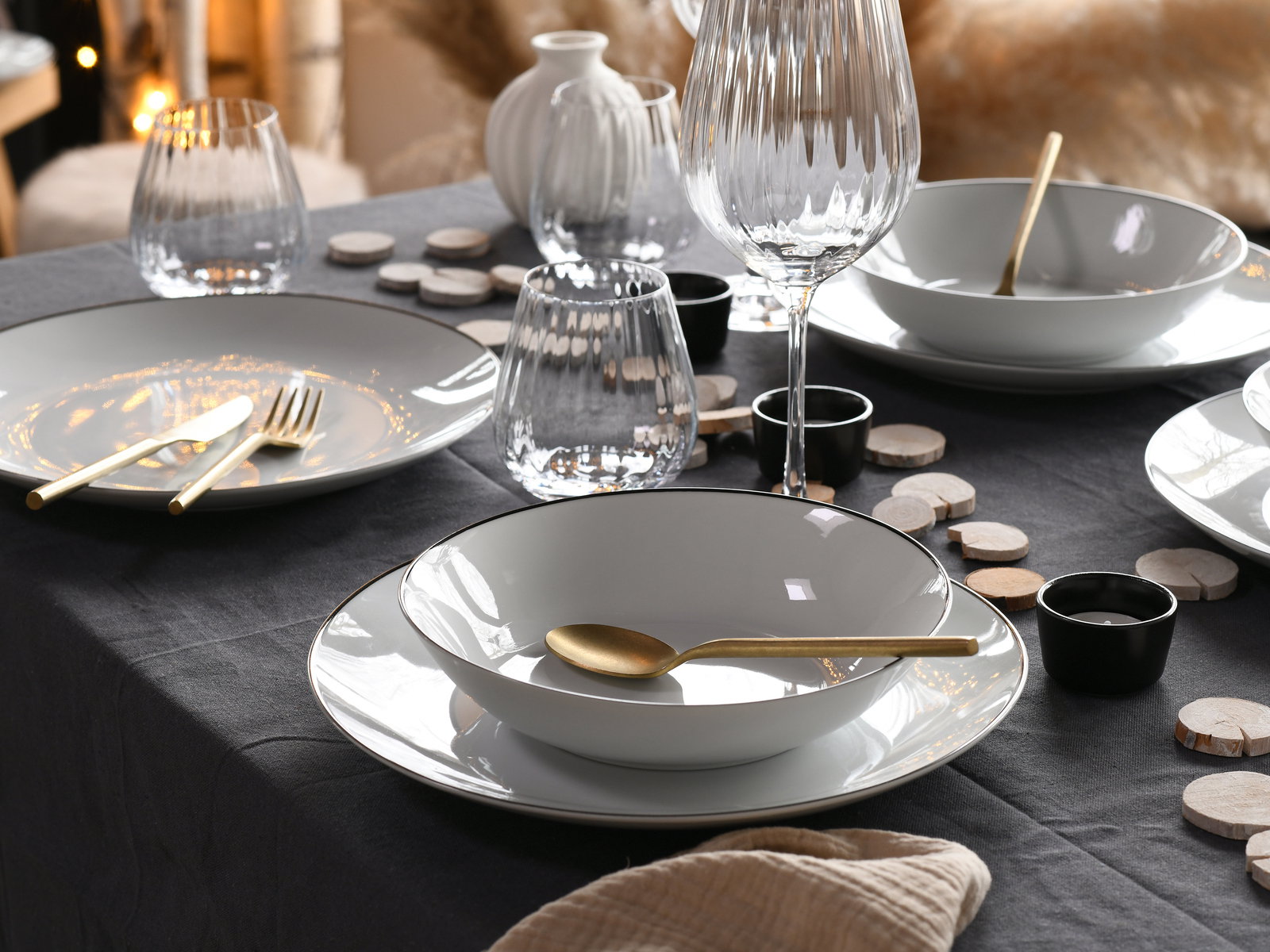 Elegantes Tellerset 18-tlg auf einem festlich gedeckten Tisch mit goldfarbenem Besteck und Gläsern, seitliche Perspektive