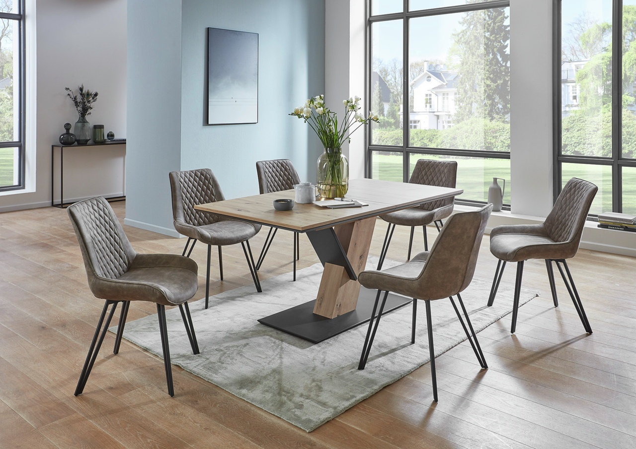 Moderner Esstisch mit Holzplatte und Metallgestell, umgeben von sechs gepolsterten Stühlen in einem hellen Raum mit großen Fenstern, seitliche Perspektive.