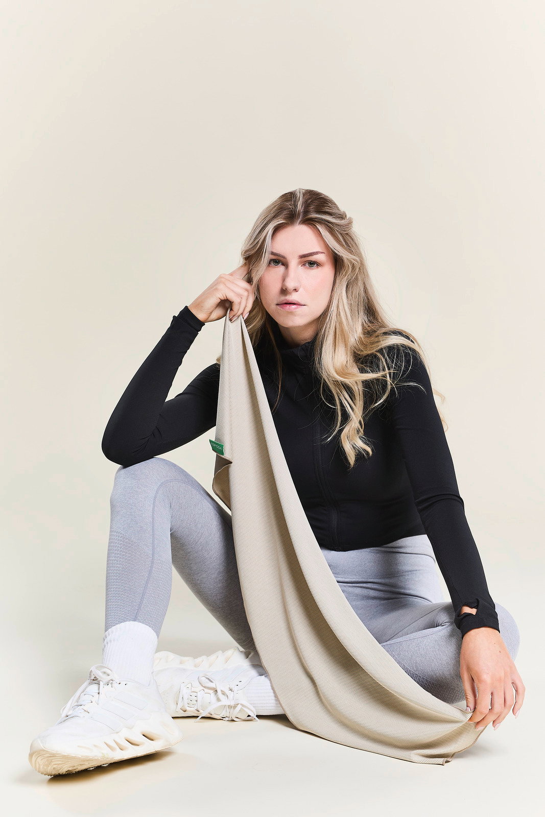 Frau in Sportkleidung hält ein beiges Sporthandtuch, sitzend in einer entspannten Pose, seitliche Perspektive