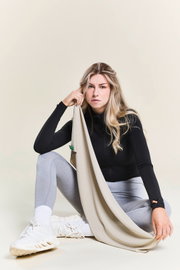 Frau in Sportkleidung hält ein beiges Sporthandtuch, sitzend in einer entspannten Pose, seitliche Perspektive