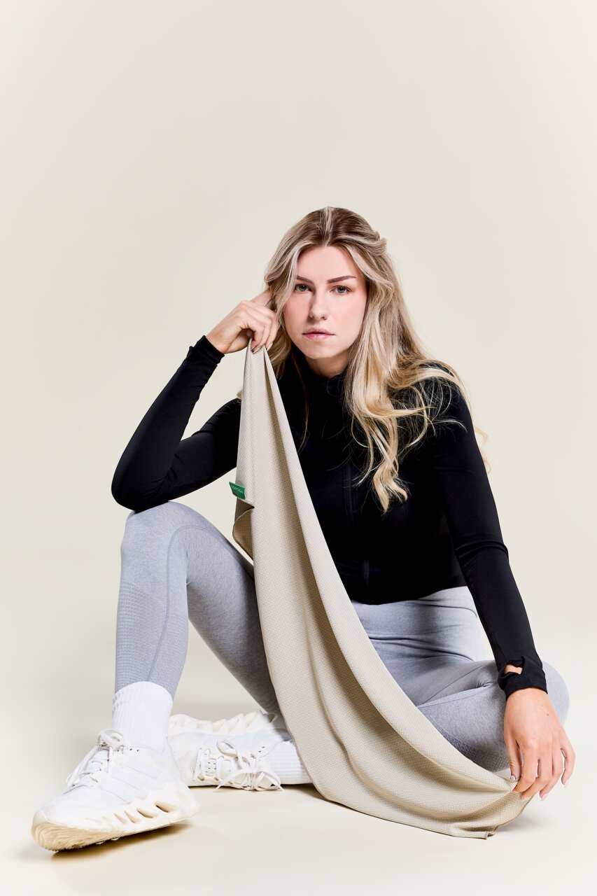 Vrouw in sportkleding houdt een beige sporthanddoek vast, zittend in een ontspannen houding, zijaanzicht