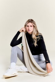 Vrouw in sportkleding houdt een beige sporthanddoek vast, zittend in een ontspannen houding, zijaanzicht