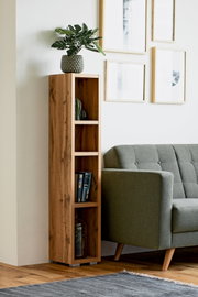 Een smalle, hoge houten kast met meerdere vakken, versierd met boeken en planten, naast een grijze bank in een moderne woonkamer. Aanzicht van voren.