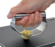 Nahaufnahme einer Hand, die eine Knoblauchpresse aus Edelstahl bedient, um frischen Knoblauch zu pressen. Die Perspektive zeigt die Presse von der Seite.