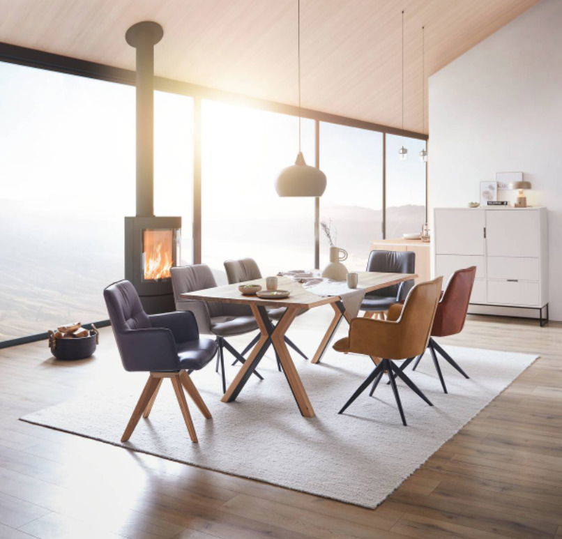Esszimmer mit modernem Design-Schalensessel in verschiedenen Farben um einen Holztisch, mit Blick auf einen Kamin und große Fenster im Hintergrund.