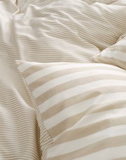 Nahaufnahme von gestreifter Bettwäsche in Beige- und Weißtönen, perspektivisch von oben fotografiert.