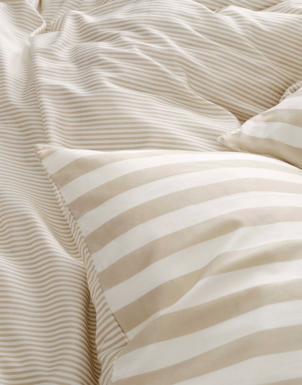 Nahaufnahme von gestreifter Bettwäsche in Beige- und Weißtönen, perspektivisch von oben fotografiert.
