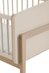 Nahaufnahme eines Anstellbetts aus Holz mit Gitterstäben und einer gepolsterten Matratze, seitliche Perspektive.