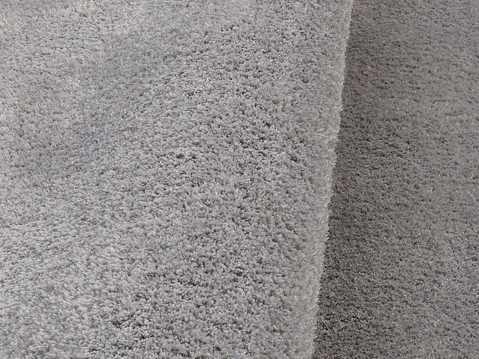 Nahaufnahme eines weichen, grauen Teppichs mit flauschiger Textur, perspektivisch von der Seite aufgenommen.