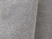 Nahaufnahme eines weichen, grauen Teppichs mit flauschiger Textur, perspektivisch von der Seite aufgenommen.