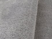 Nahaufnahme eines weichen, grauen Teppichs mit flauschiger Textur, perspektivisch von der Seite aufgenommen.